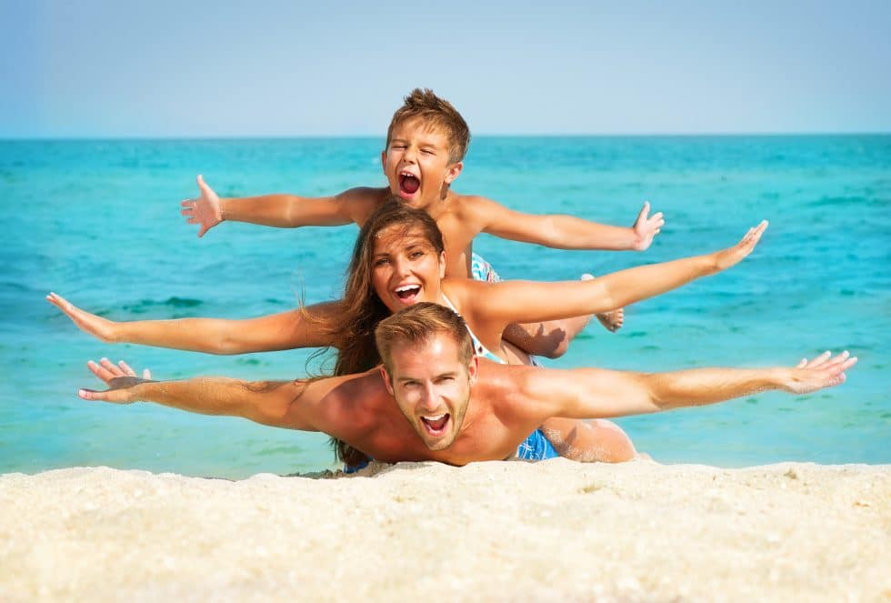 Vacation Travel Innovation Reviews family beach image showing parents and a child enjoying a playful vacation moment.